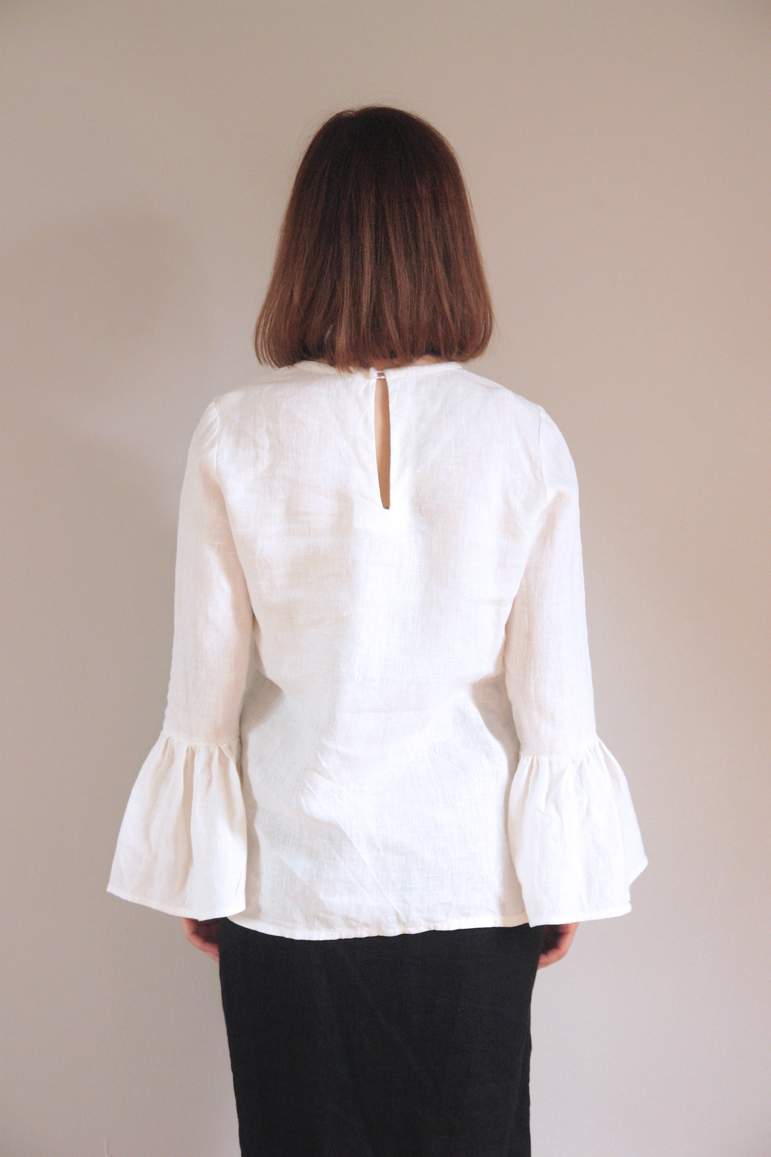 Versatile white linen blouse featuring voluminous bell sleeves and a clean round neckline. The breathable fabric and relaxed silhouette make it ideal for both casual and formal occasions
