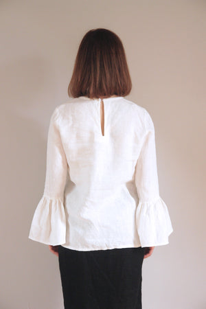 Versatile white linen blouse featuring voluminous bell sleeves and a clean round neckline. The breathable fabric and relaxed silhouette make it ideal for both casual and formal occasions