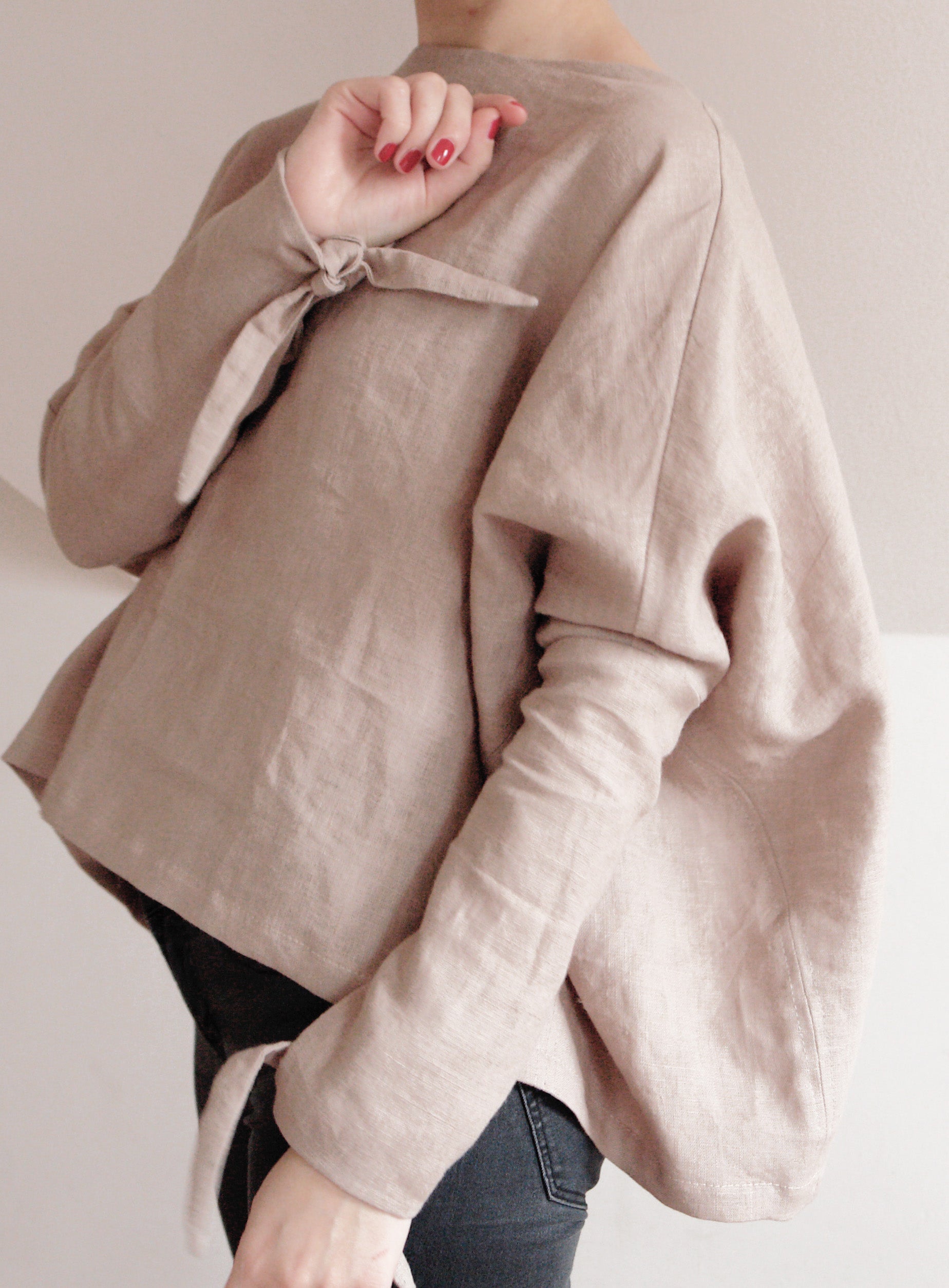 Minimalist linen kimono-style top in a neutral beige tone. Features long sleeves with delicate tie details at the wrists and a relaxed, oversized fit. Made from breathable, high-quality linen for effortless comfort and style