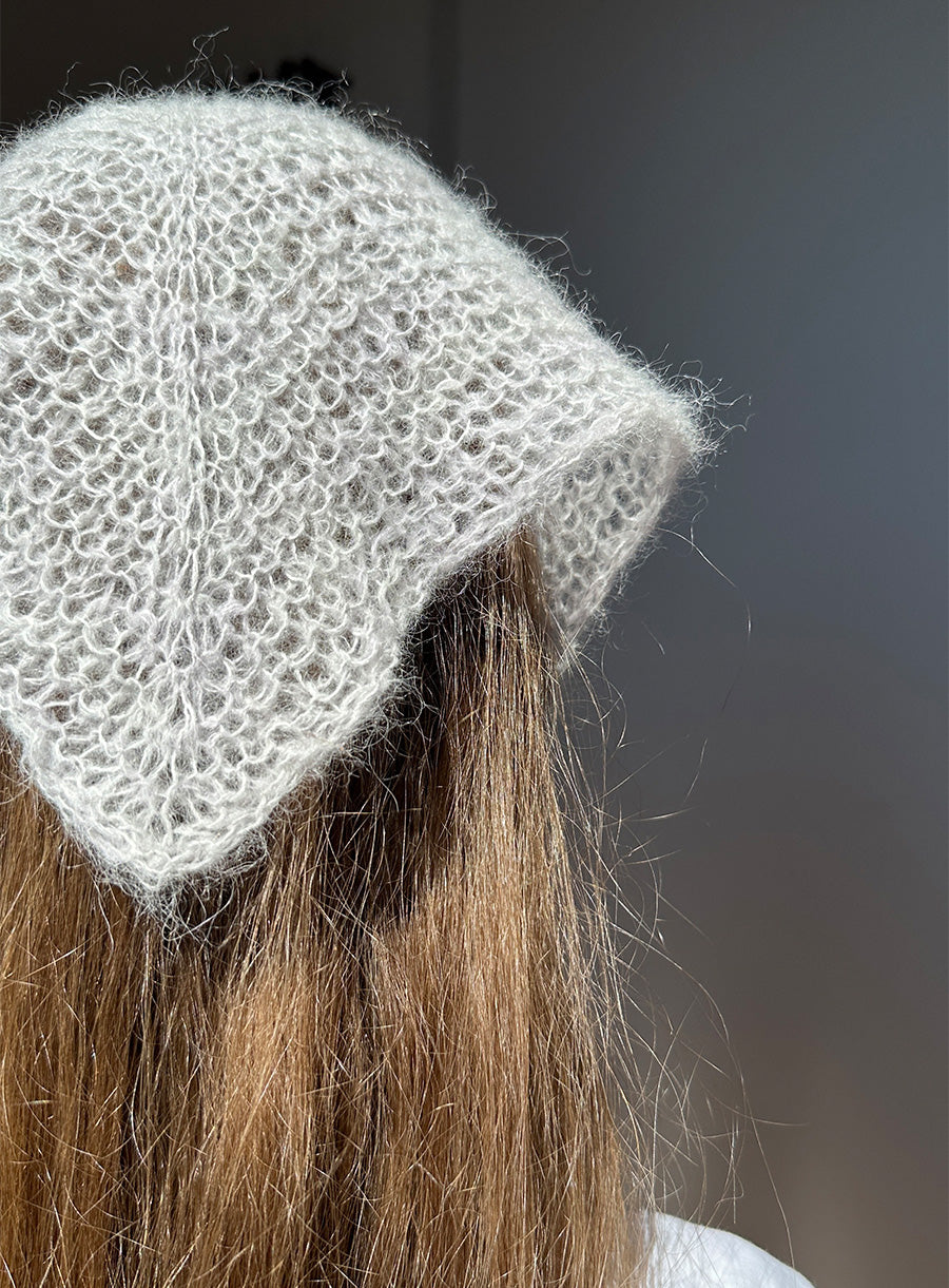 Close-up of a person wearing a textured white knit bandana hat against a dark background