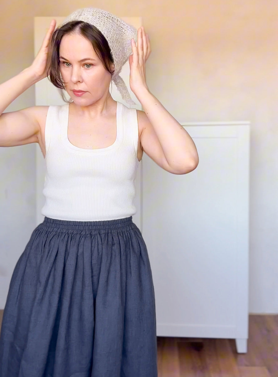 Woman wearing a white tank top and dark blue skirt indoors.
