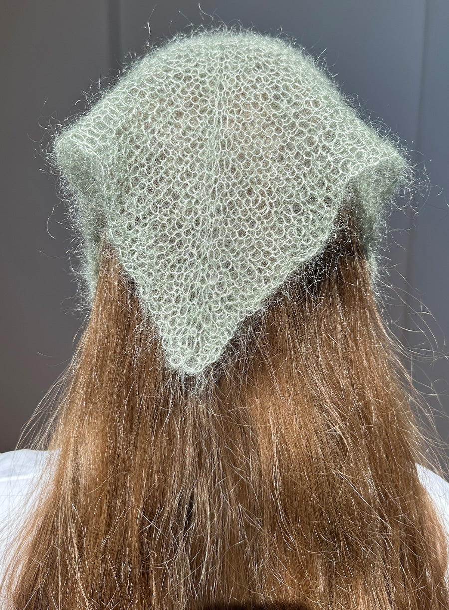 Light green knitted hat on a person with long brown hair against a neutral background