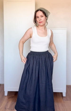 Woman wearing a white tank top and navy blue skirt indoors.