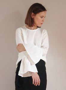 Elegant white linen blouse with dramatic frill sleeves, worn by a woman with a sleek bob haircut. The blouse features a relaxed fit and round neckline, styled with a black skirt for a modern minimalist look.