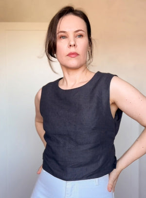 Minimalist sleeveless linen blouse in dark charcoal, featuring an adjustable tie-back detail for a flattering fit.