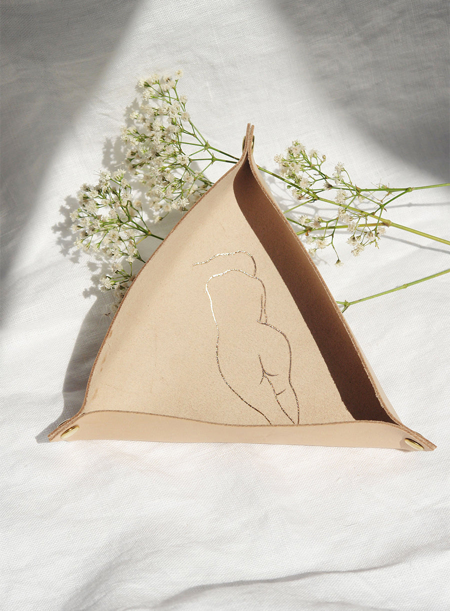 Minimalist genuine leather tray with gold-engraved abstract female silhouette. Handcrafted, soft beige leather with brass snap fasteners. Perfect for organizing small essentials. Styled with delicate white florals on linen fabric.