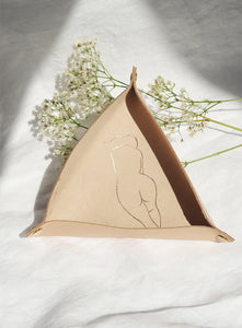 Minimalist genuine leather tray with gold-engraved abstract female silhouette. Handcrafted, soft beige leather with brass snap fasteners. Perfect for organizing small essentials. Styled with delicate white florals on linen fabric.