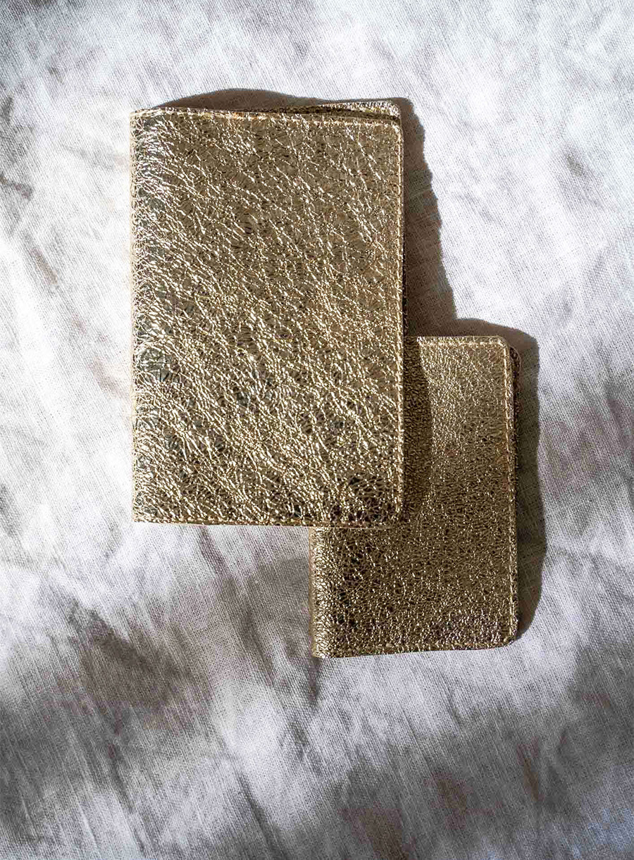 A stylish gold passport wallet designed for travelers, featuring a smooth surface and durable edges, placed on a neutral-toned backdrop