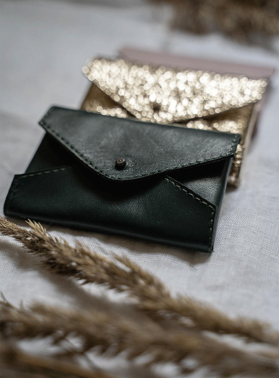 Gold envelope-shaped cardholder with a unique textured finish, displayed on dried wheat stems against a dark green background – a blend of style and sustainability.