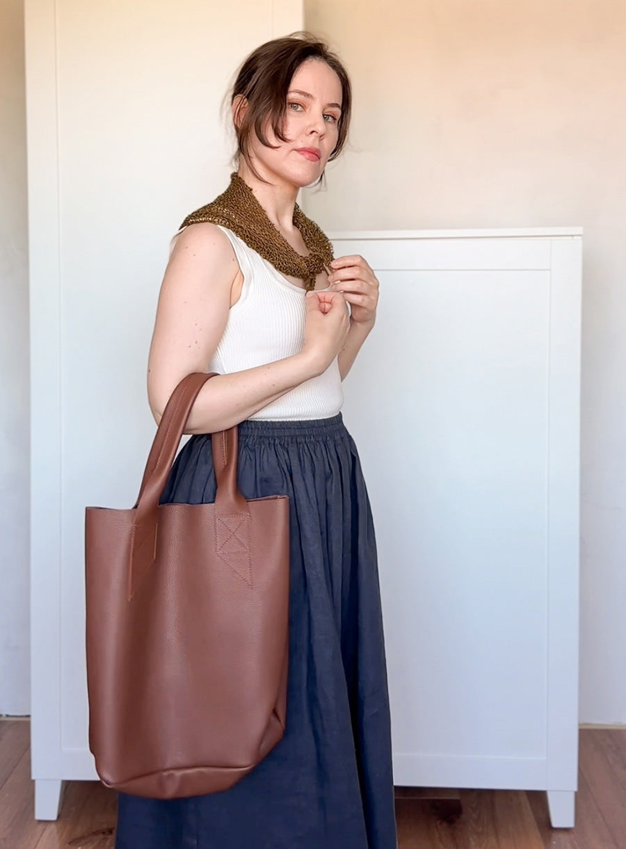 Woman holding a brown leather tote bag with linen scarf
