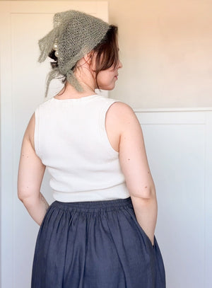 Person wearing a white sleeveless top and blue skirt with a green knitted headscarf.