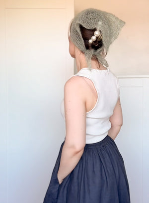 Person wearing a white sleeveless top and dark blue skirt with a gray knitted headscarf.