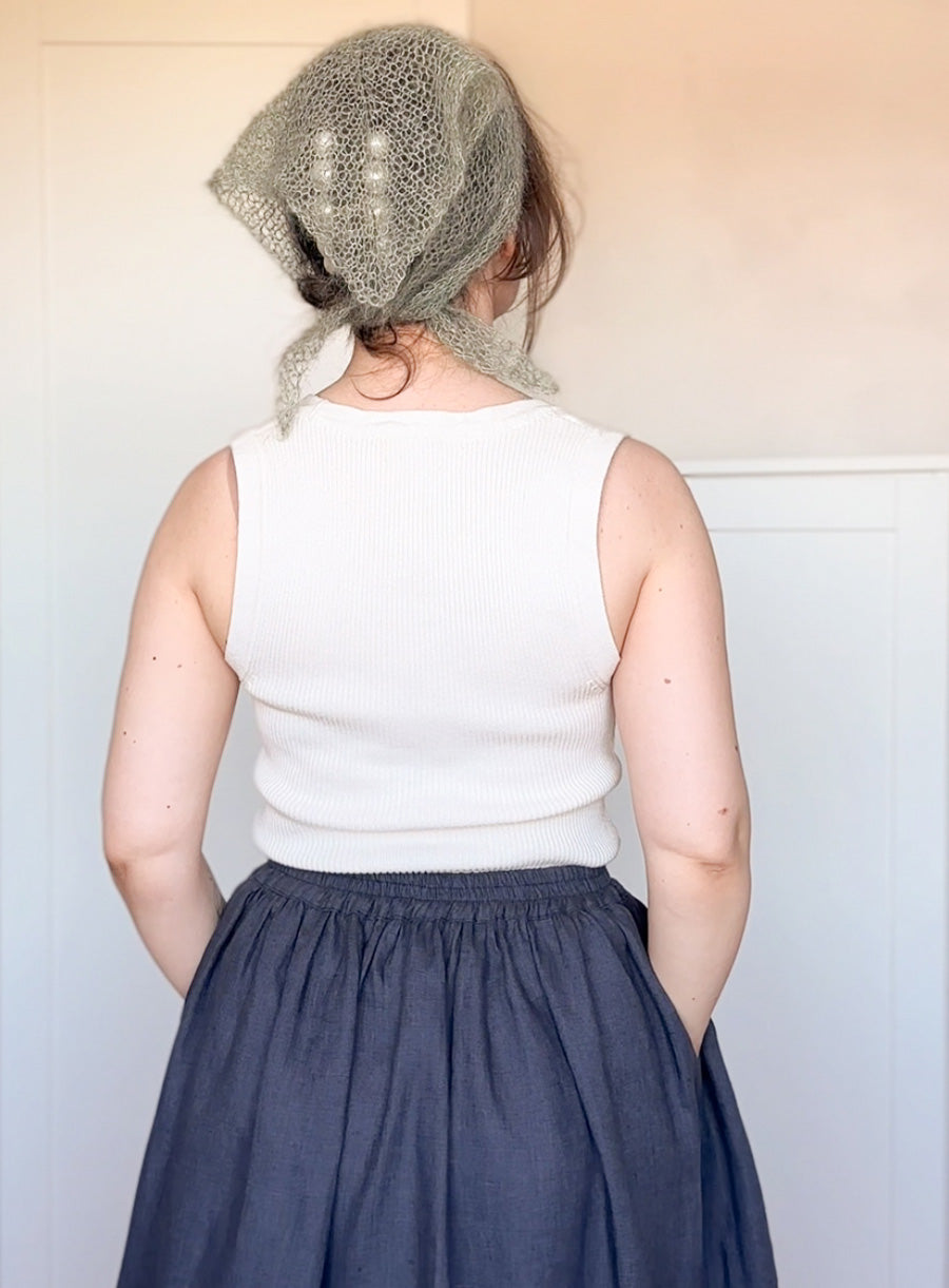 Person wearing a white sleeveless top and dark blue skirt with a textured headscarf.