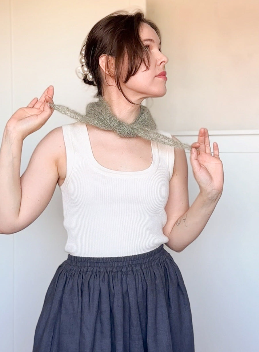 Woman wearing a white tank top and dark blue skirt with a green knitted scarf.