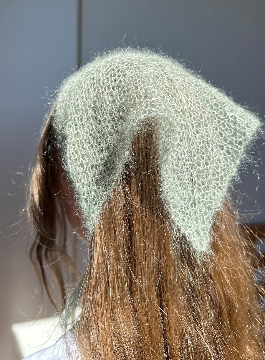 Light green knitted headband on a person with brown hair against a neutral background