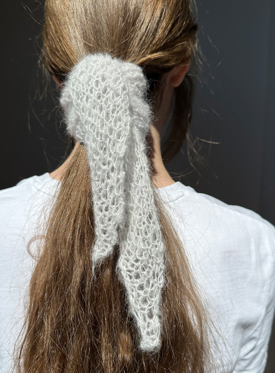 Person with a knitted white hair accessory in their hair against a dark background