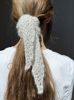 Person with a knitted white hair accessory in their hair against a dark background
