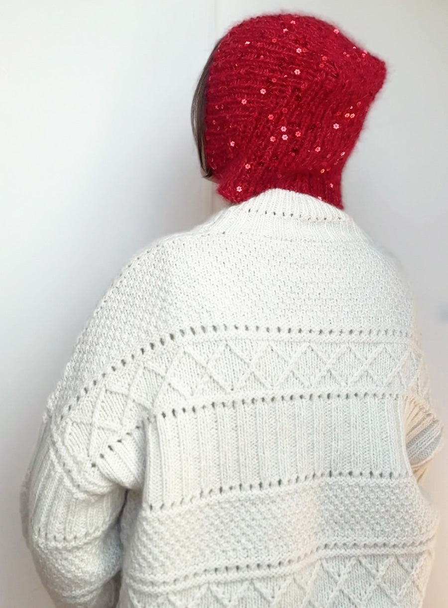 Cozy and elegant handmade red knit bonnet with sparkling sequins, styled on a model in a white sweater. Perfect for Halloween or Christmas gift ideas.