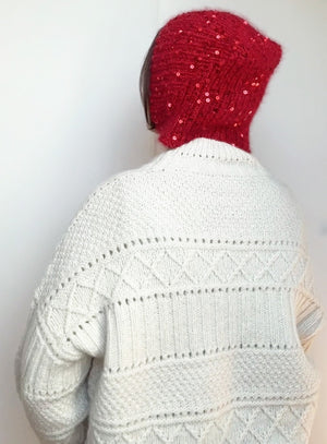 Cozy and elegant handmade red knit bonnet with sparkling sequins, styled on a model in a white sweater. Perfect for Halloween or Christmas gift ideas.