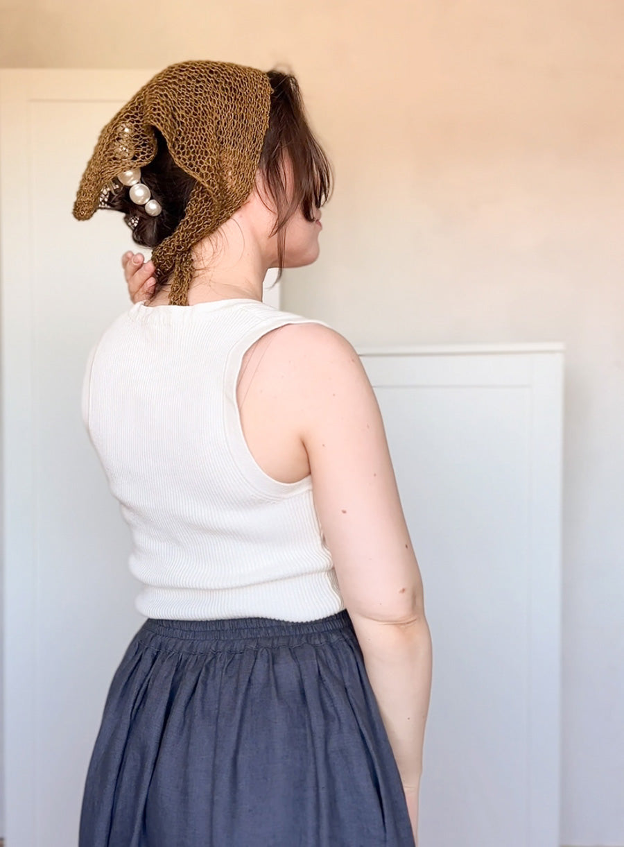 Person wearing a grenn linen knitted bonnet with pearls, standing against a plain background