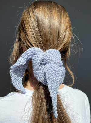Person with a blue knitted hair accessory in their hair against a dark background
