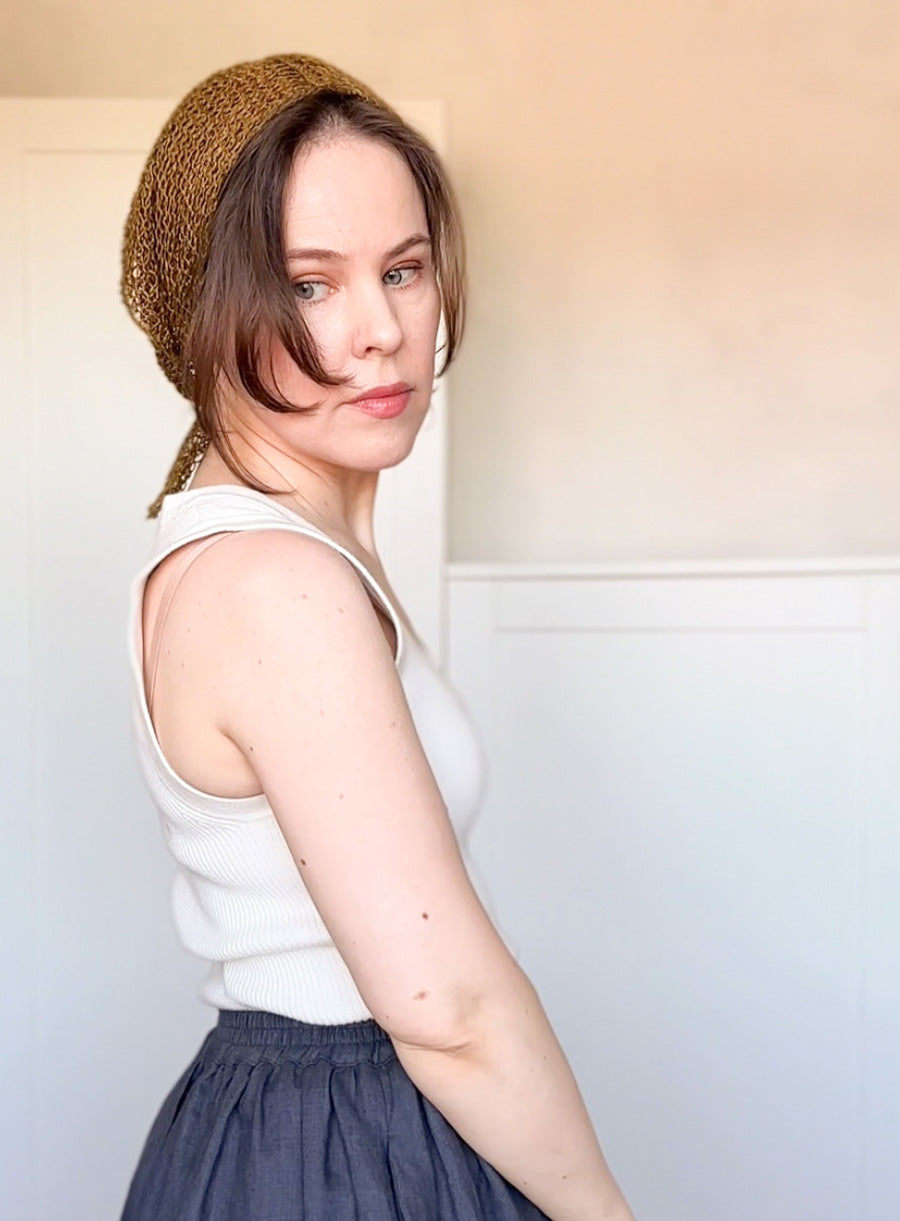 Woman wearing a white sleeveless top and dark skirt with a brown knitted headband against a light background