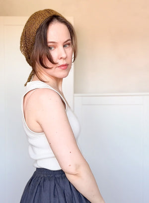Woman wearing a white sleeveless top and dark skirt with a brown knitted headband against a light background