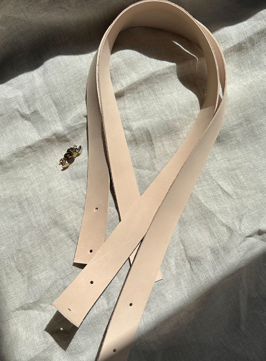 Set of two natural vegetable-tanned leather handles with pre-punched holes, perfect for DIY bag-making, furniture handles, or craft projects. Includes matching brass hardware. Soft, unfinished edges for a customizable look. Sunlit on neutral fabric background.
