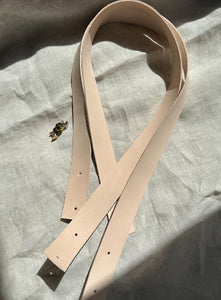 Set of two natural vegetable-tanned leather handles with pre-punched holes, perfect for DIY bag-making, furniture handles, or craft projects. Includes matching brass hardware. Soft, unfinished edges for a customizable look. Sunlit on neutral fabric background.