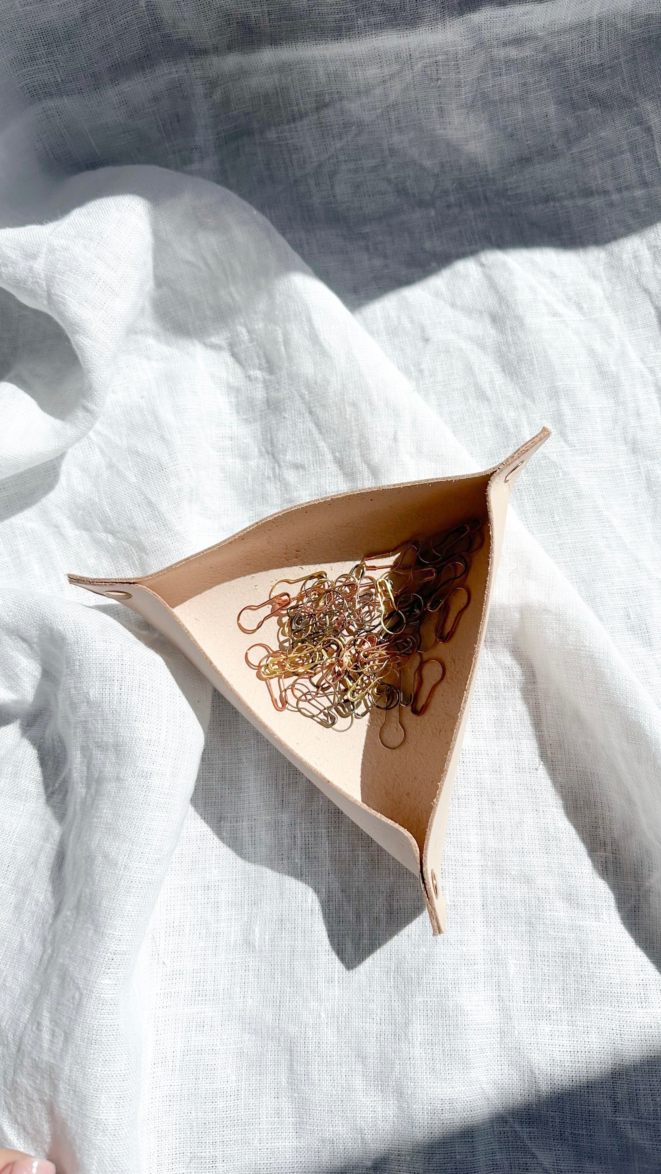 Minimalist leather valet tray in natural beige, holding gold and silver stitch markers, displayed in soft natural light
