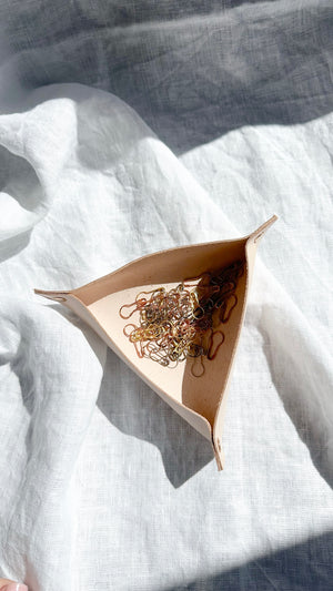Minimalist leather valet tray in natural beige, holding gold and silver stitch markers, displayed in soft natural light