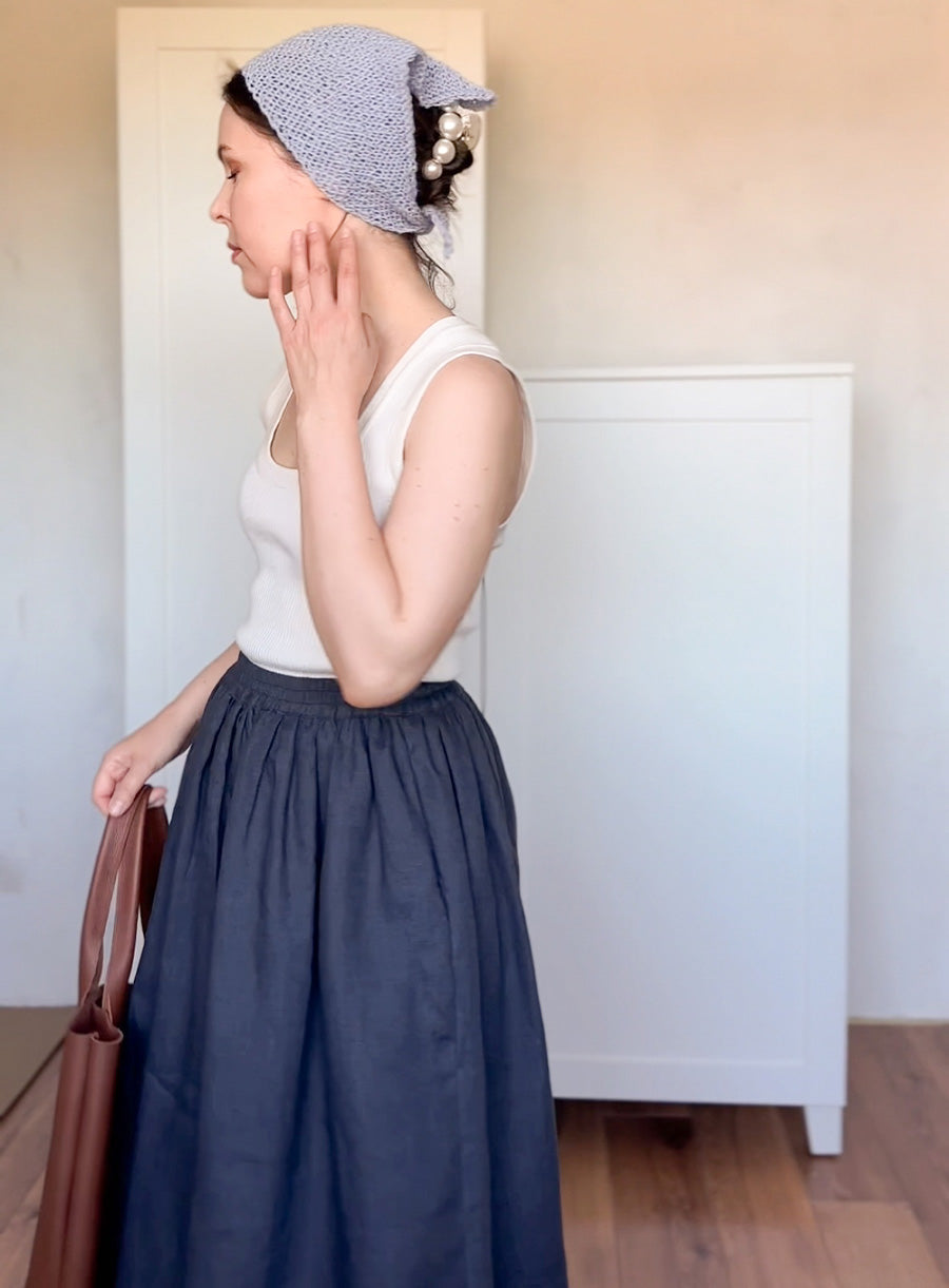 Woman wearing a white top and blue skirt with a headscarf, standing indoors.