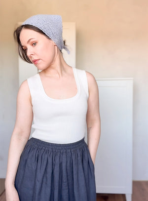Woman wearing a white tank top and blue skirt with a light blue headscarf indoors.