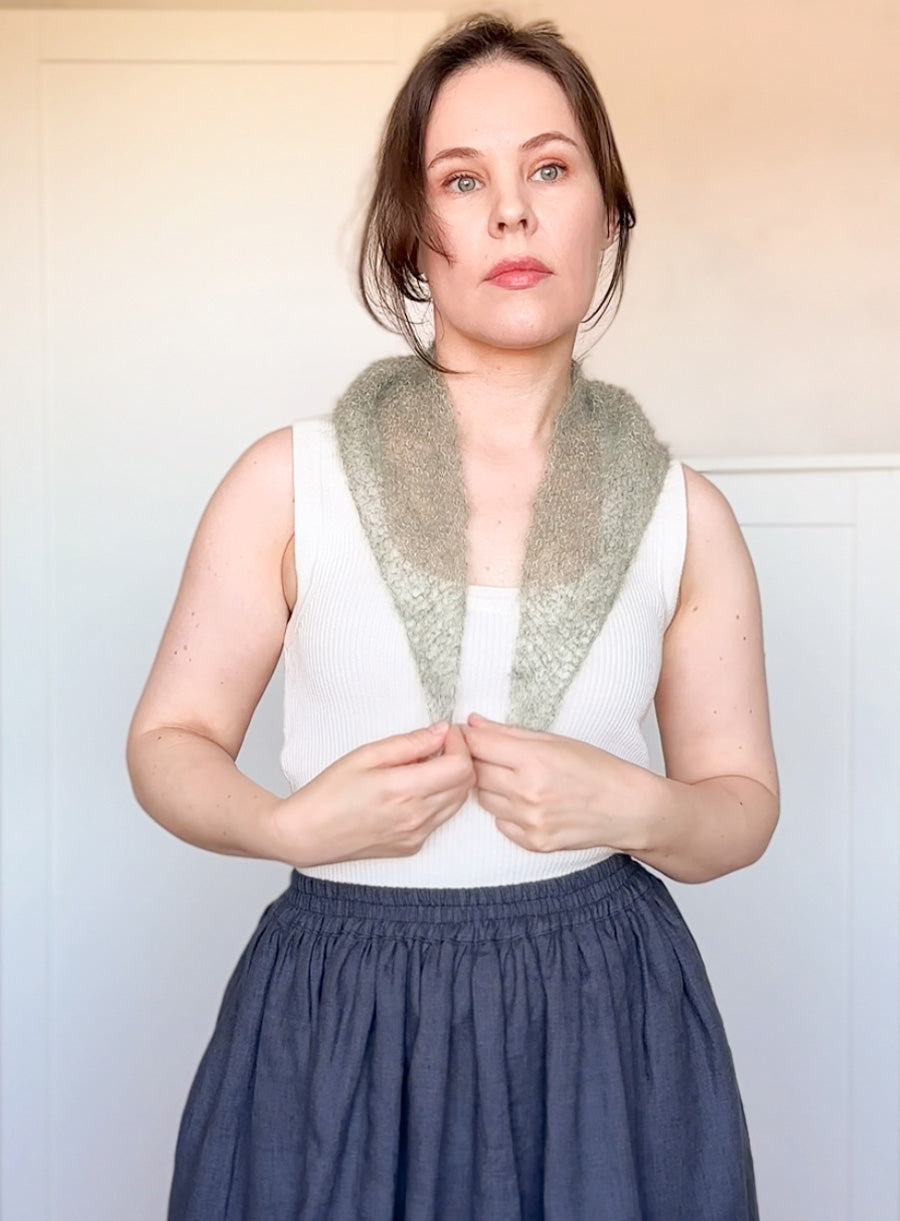 Woman wearing a white sleeveless top with a green knitted scarf against a plain background