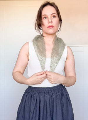 Woman wearing a white sleeveless top with a green knitted scarf against a plain background