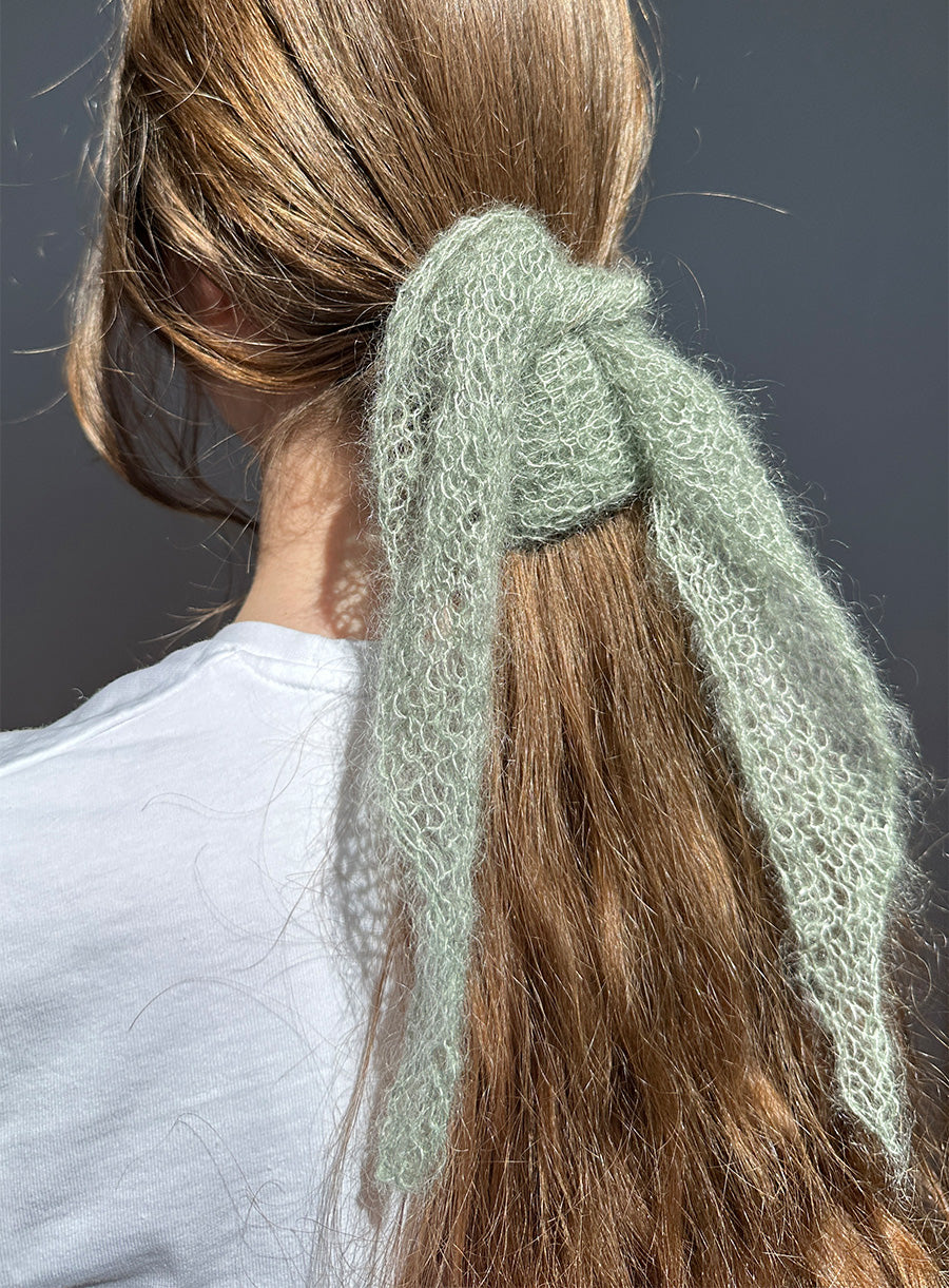 Person with a green knitted hairband in their brown hair against a dark background