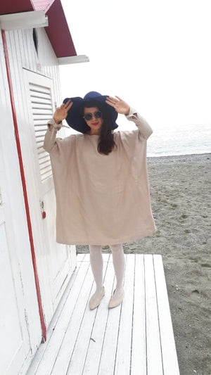 Oversized beige linen dress with wide sleeves, styled with white leggings, a navy blue hat, and round sunglasses. Lightweight, relaxed, and effortlessly chic.