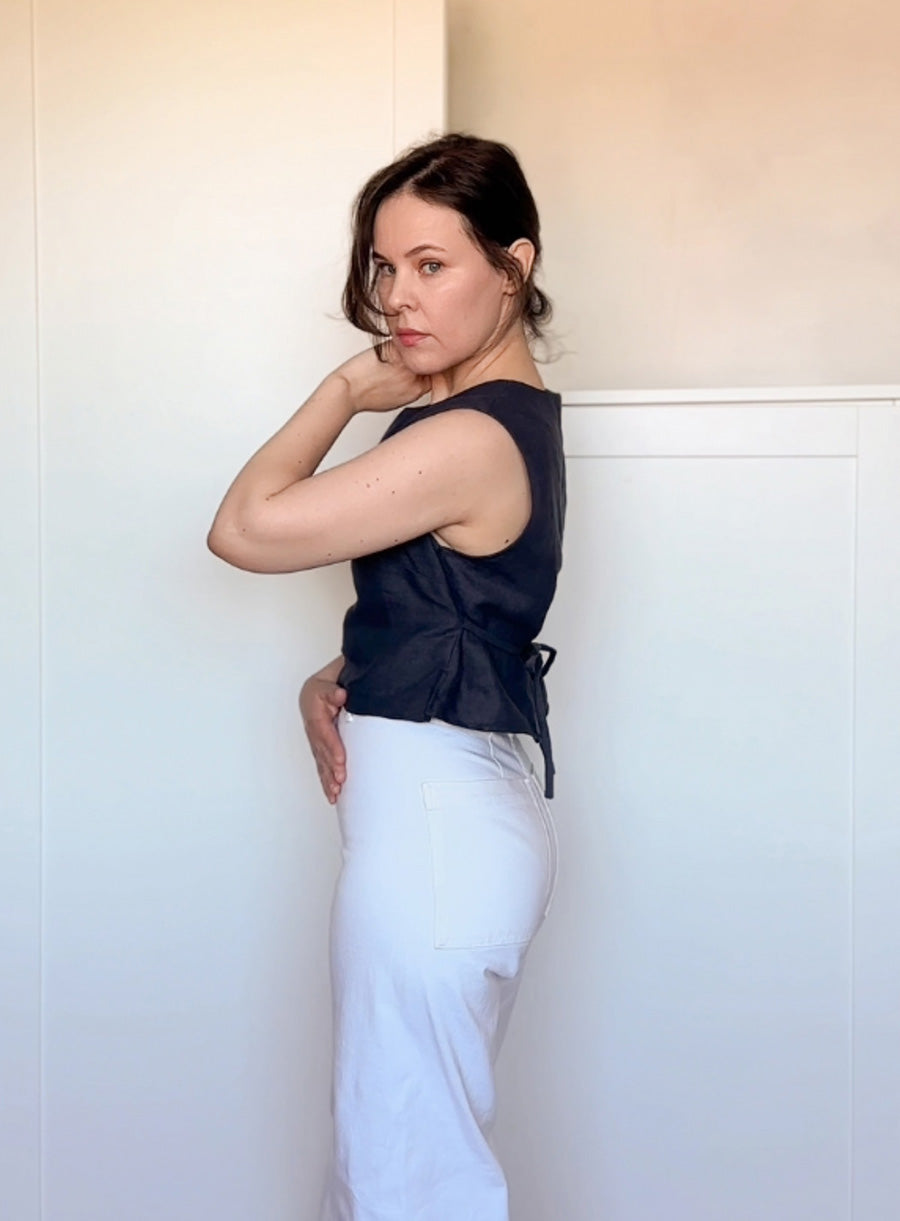 Side view of a fitted black linen sleeveless blouse with a wrap-around tie belt and structured silhouette