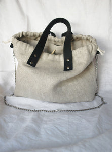 Linen knitting project bag made from high-quality heavy linen fabric, featuring a stylish herringbone pattern. Designed with sturdy black leather handles, a secure drawstring closure, and a silver chain strap for versatile carrying options. Perfect for storing and transporting knitting or crochet projects with elegance and durability
