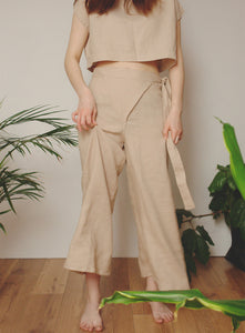 Minimalist beige linen outfit featuring a cropped top and wrap pants, styled in a natural indoor setting with greenery.