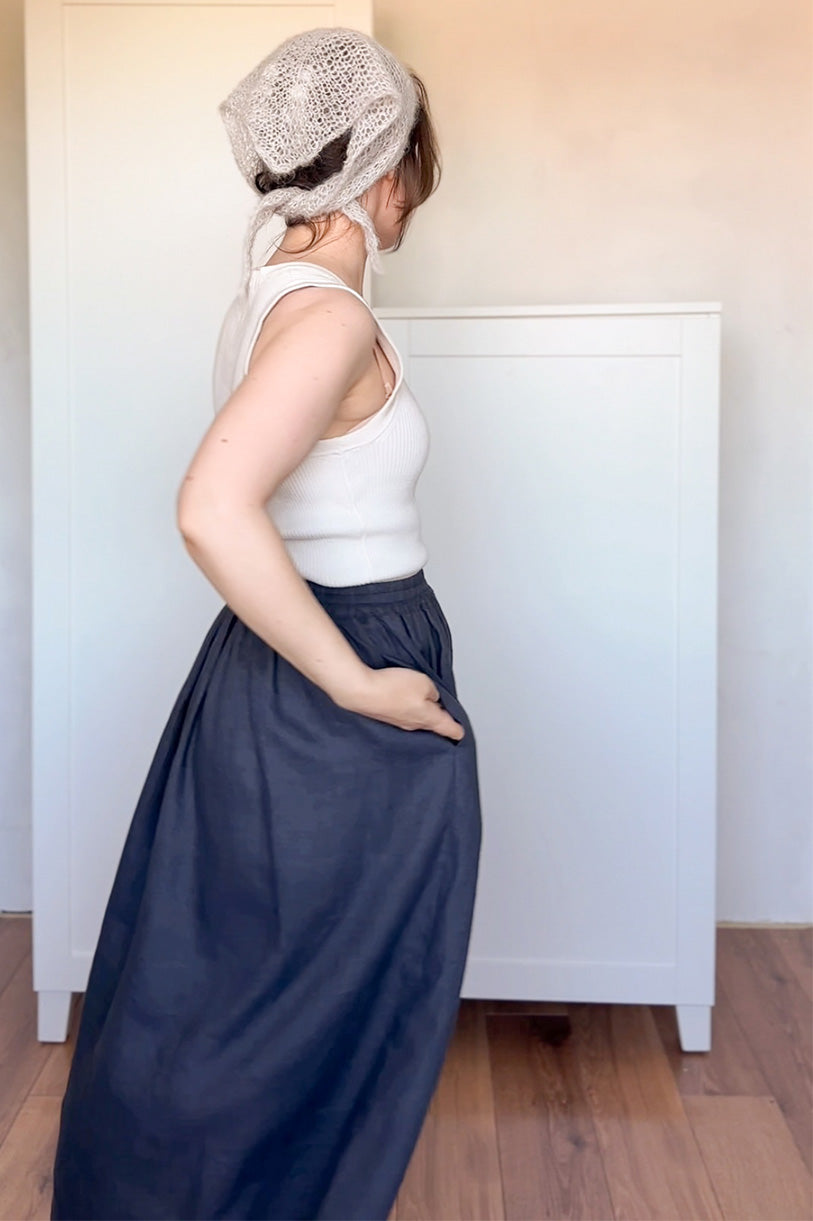 Person wearing a white top and navy skirt with a textured headscarf indoors.