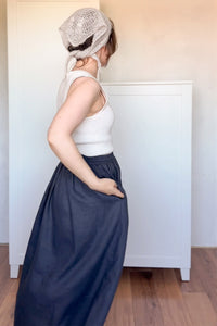 Person wearing a white top and navy skirt with a textured headscarf indoors.