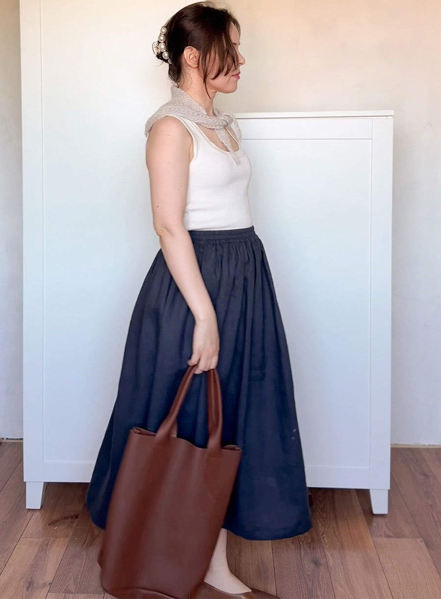 Woman wearing a white top and navy skirt holding a brown bag and mohair bandana