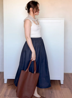 Woman wearing a white top and navy skirt holding a brown bag and mohair bandana