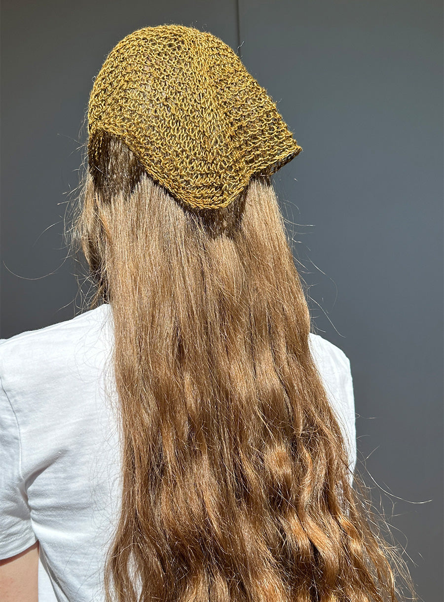 Person wearing a green knitted headband with long hair against a gray background