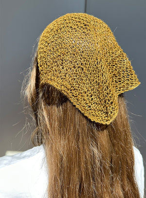 Linen green knitted hat worn by a person with long hair against a neutral background