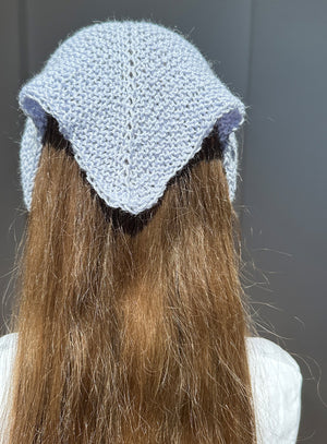 Person wearing a light blue knitted headband with a dark interior against a neutral background