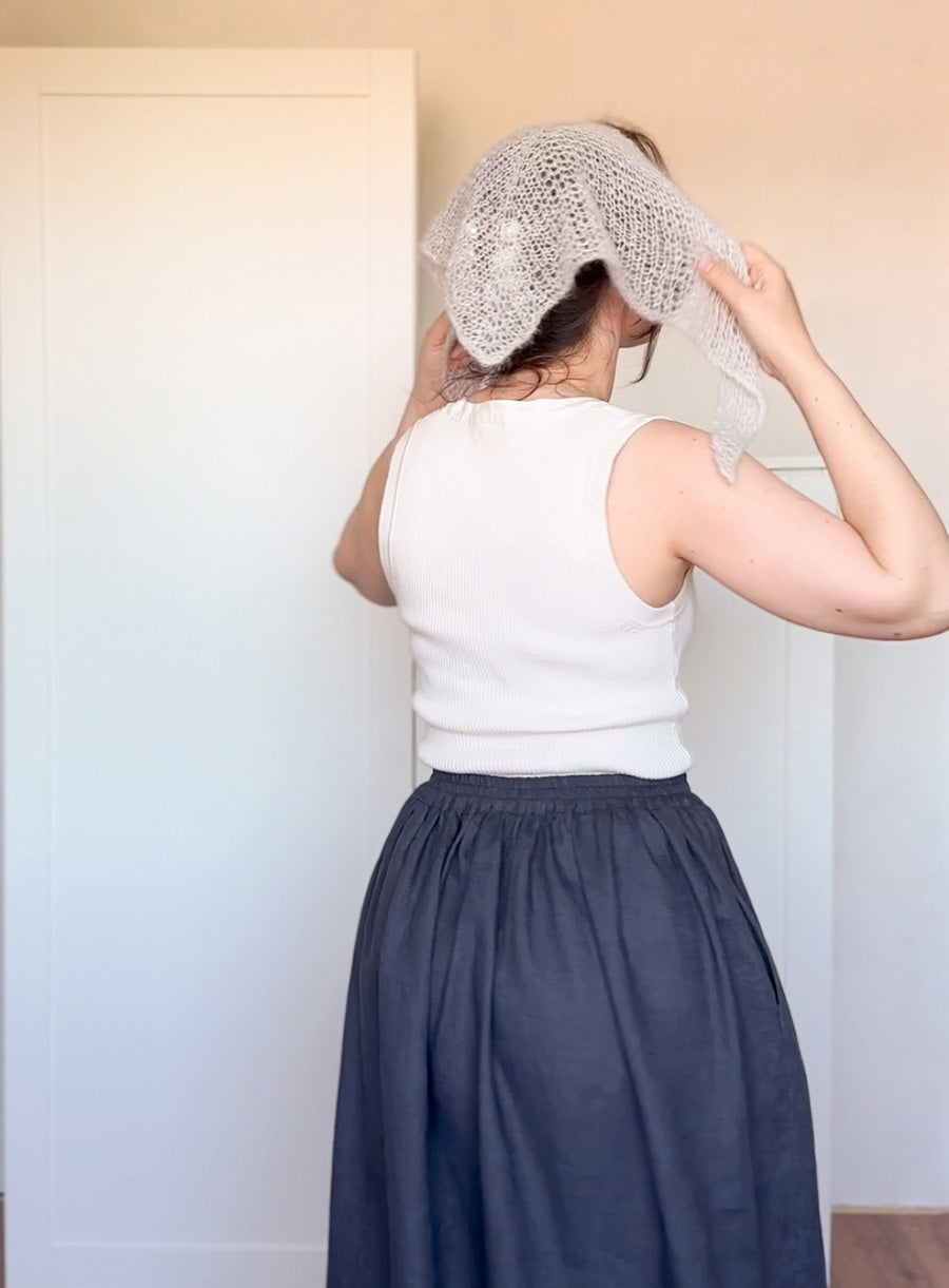 Person wearing a white sleeveless top and navy skirt with a textured headscarf.