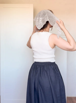 Person wearing a white sleeveless top and navy skirt with a textured headscarf.