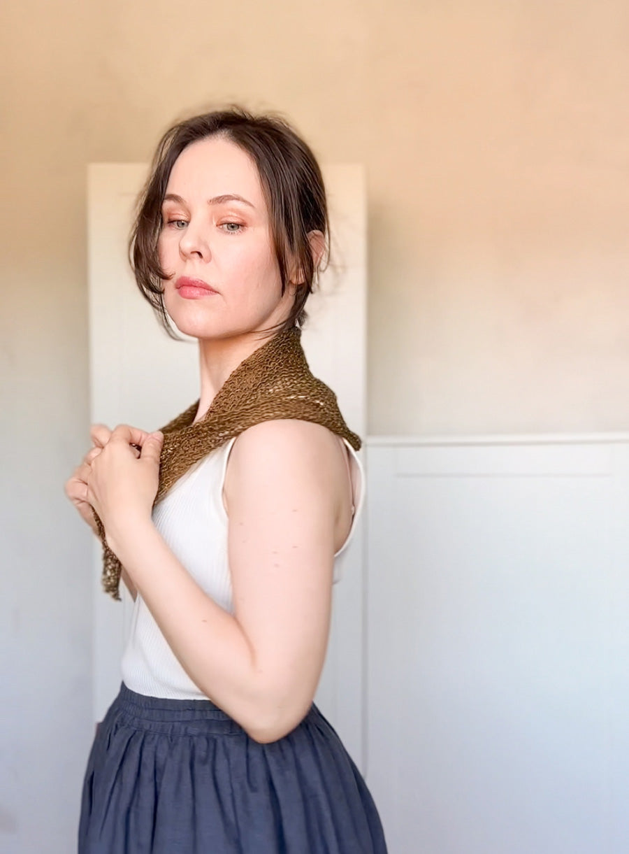 Woman wearing a knitted green linen scarf against a plain background